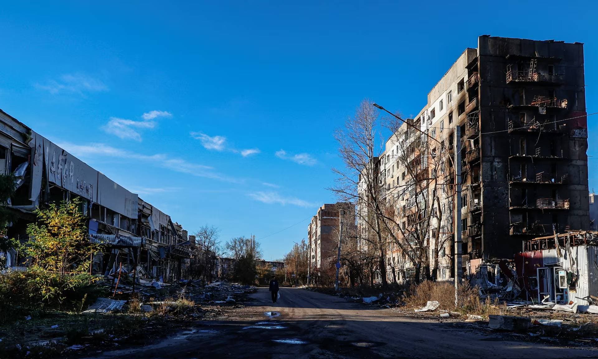 A person walks next to hollowed-out buildings, heavily damaged by Russian strikes on the frontline town of Avdiivka