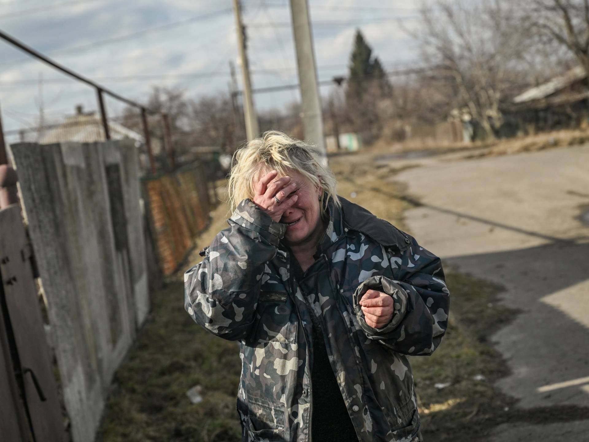 A woman reacts to the sound of shelling as she stands outside her house in the village of Chasiv Yar