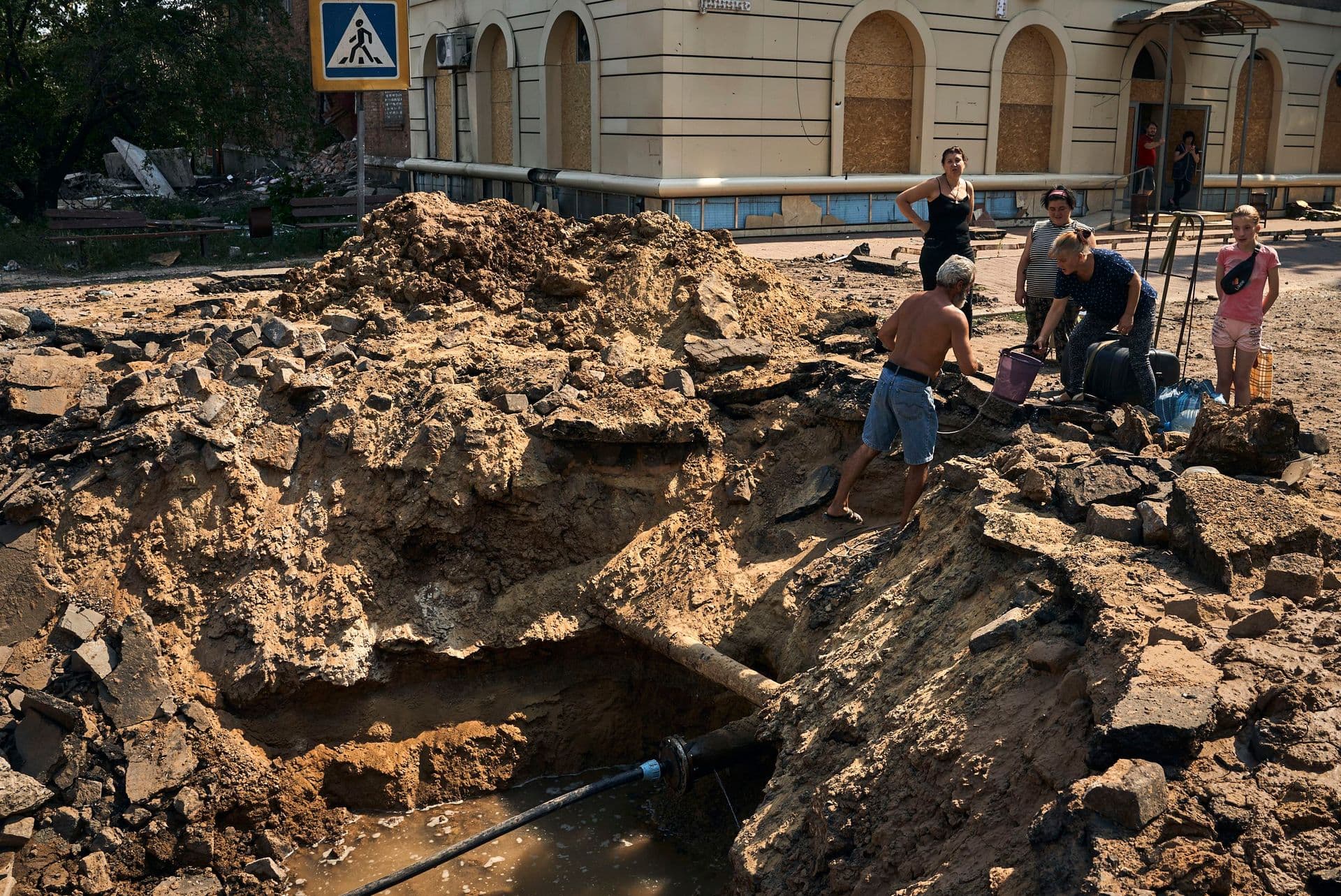 Local residents take water from a partially restored water supply in a crater after an air bomb hit in Bakhmut