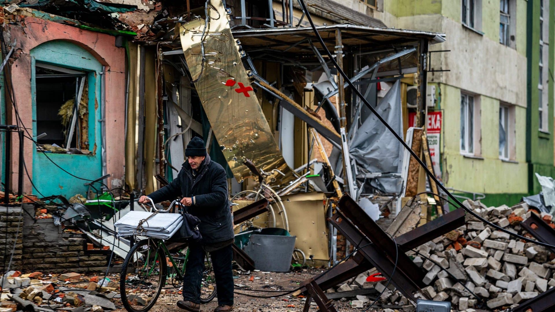 A local resident pushes his bicycle past 'hedgehog' tank traps and rubble down a street in Bakhmut