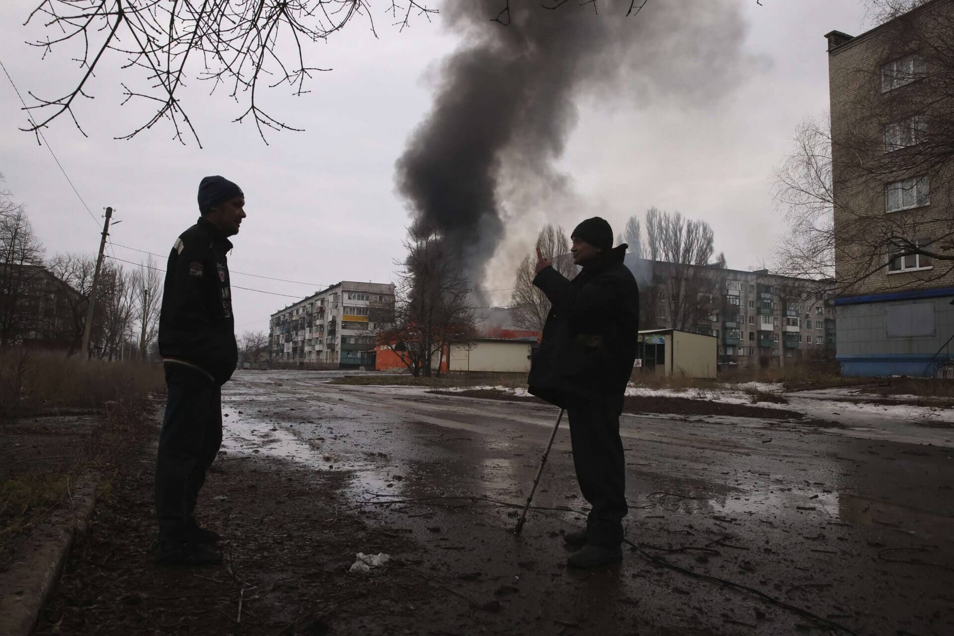 Local residents talk against the background of a building burning after the Russian shelling in the town of Chasiv Yar