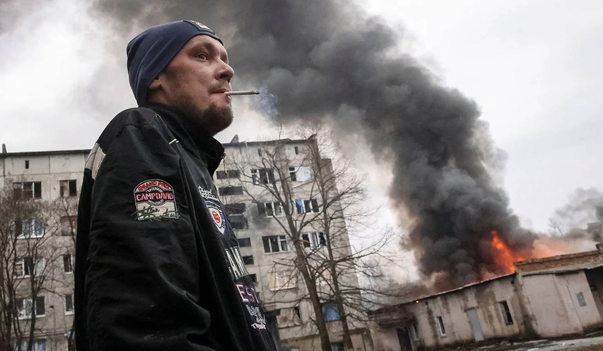 A local resident smokes near a buildings damaged by a Russian military strike in Chasiv Yar