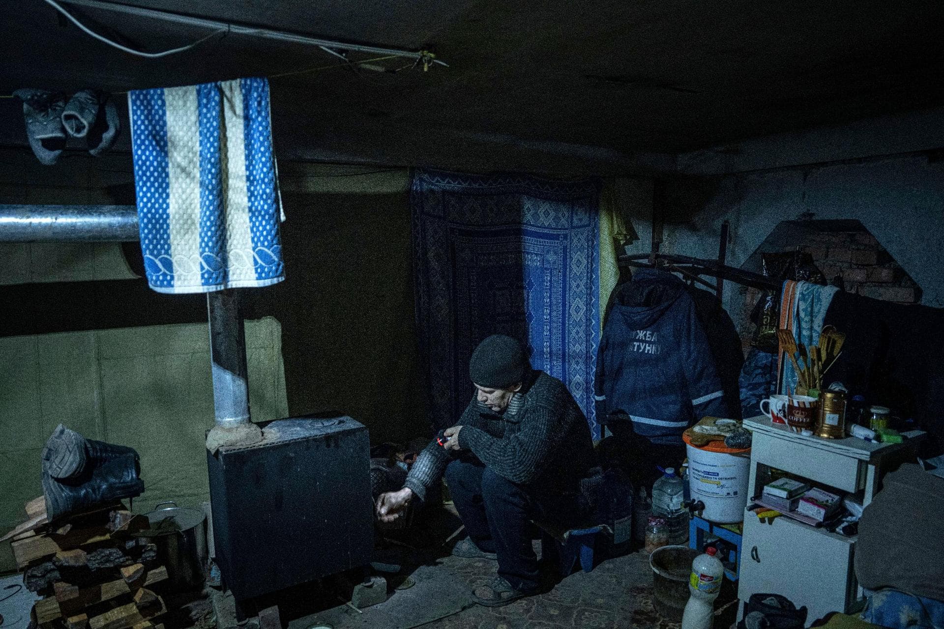 Leonid places wood into a potbelly stove as he continues to live in the city without electricity, running water and gas in Siversk