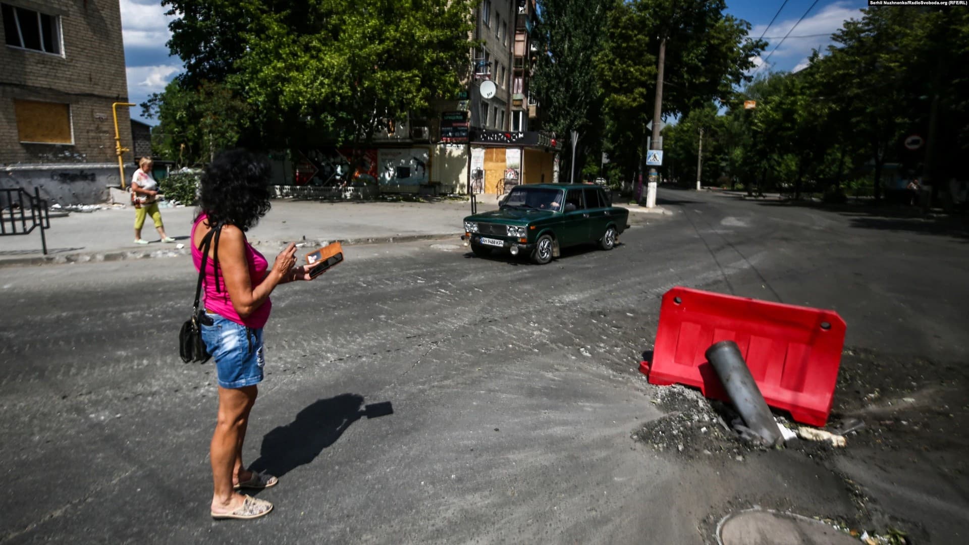A woman photographs the remains of a missile that struck a road