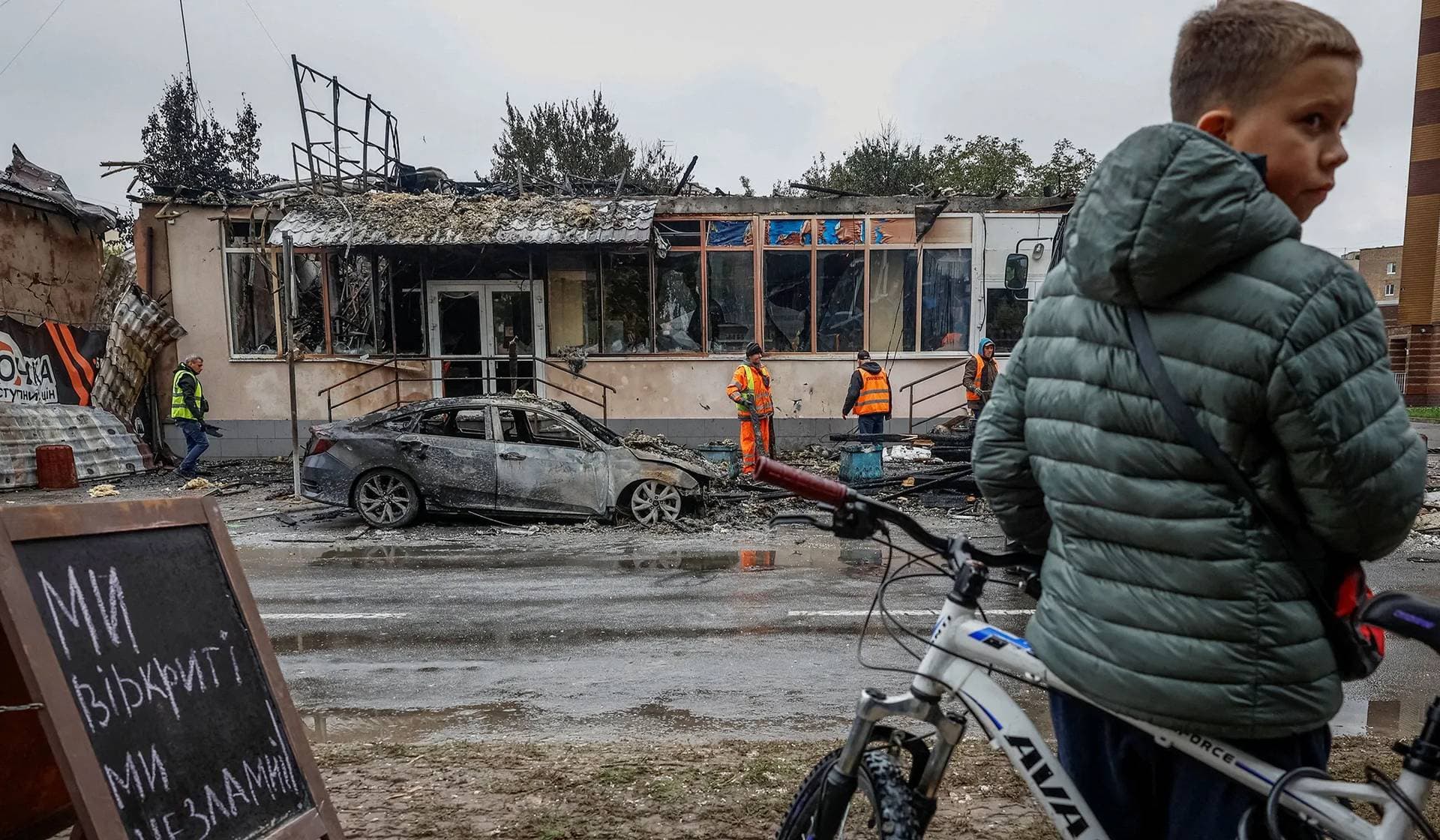 A boy with a bicycle looks on near buildings damaged during a Russian drone and missile strike in Brovary