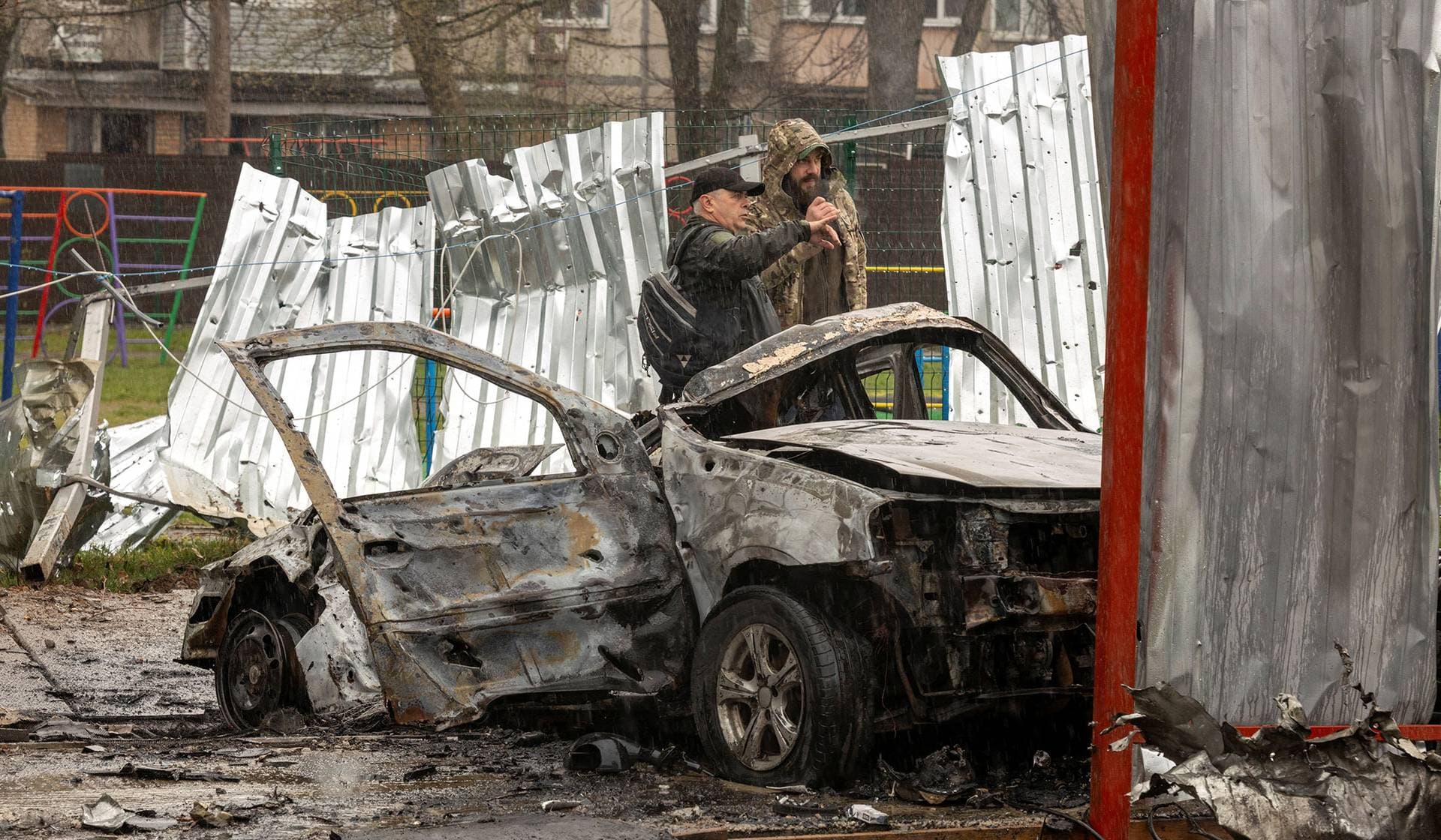 Men stand next to a burned car at the impact site of a Russian drone in a residential neighborhood in Vyshneve