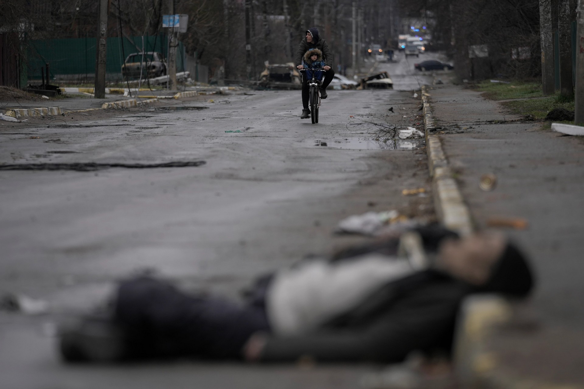 A man and a child on a bicycle come across the body of a civilian lying on the street