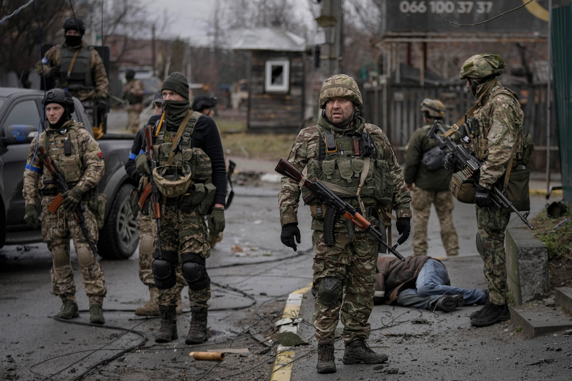 Ukrainian servicemen stand next to the body of a man in civilian clothing
