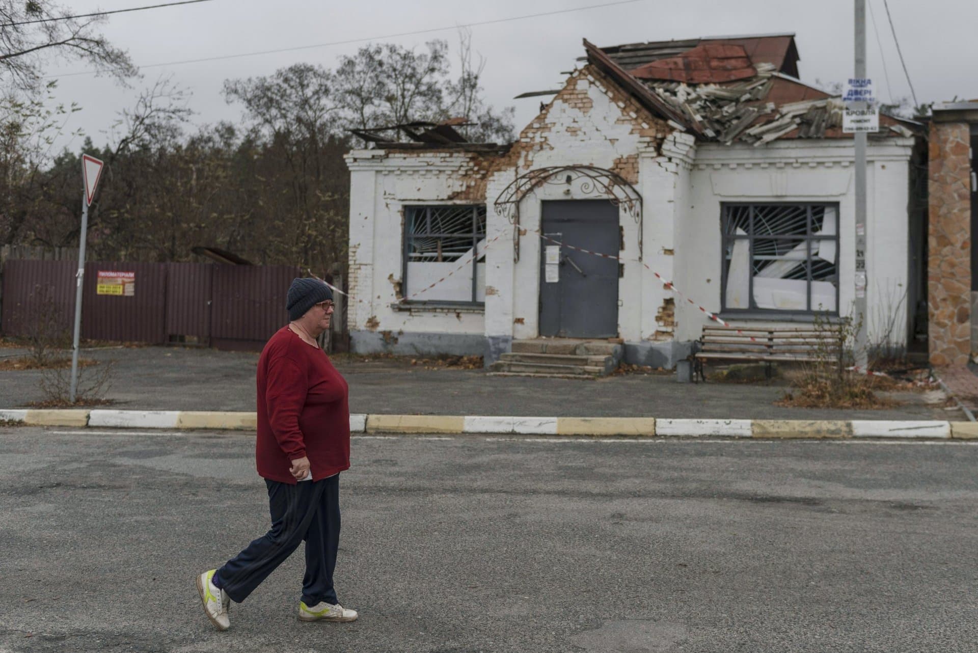 A woman passes an apartment building destroyed by fighting, in the village of Moshun