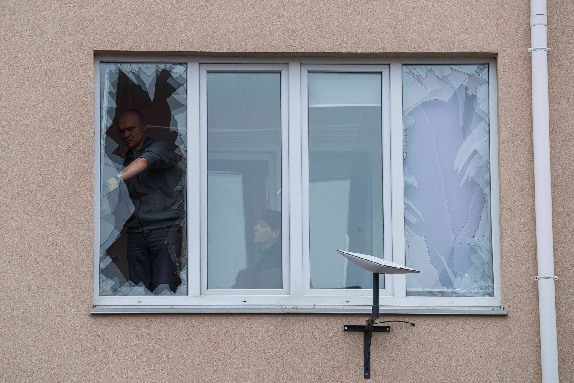 People remove broken glass from their windows after a Russian strike on residential neighbourhood in Kriukivshchyna