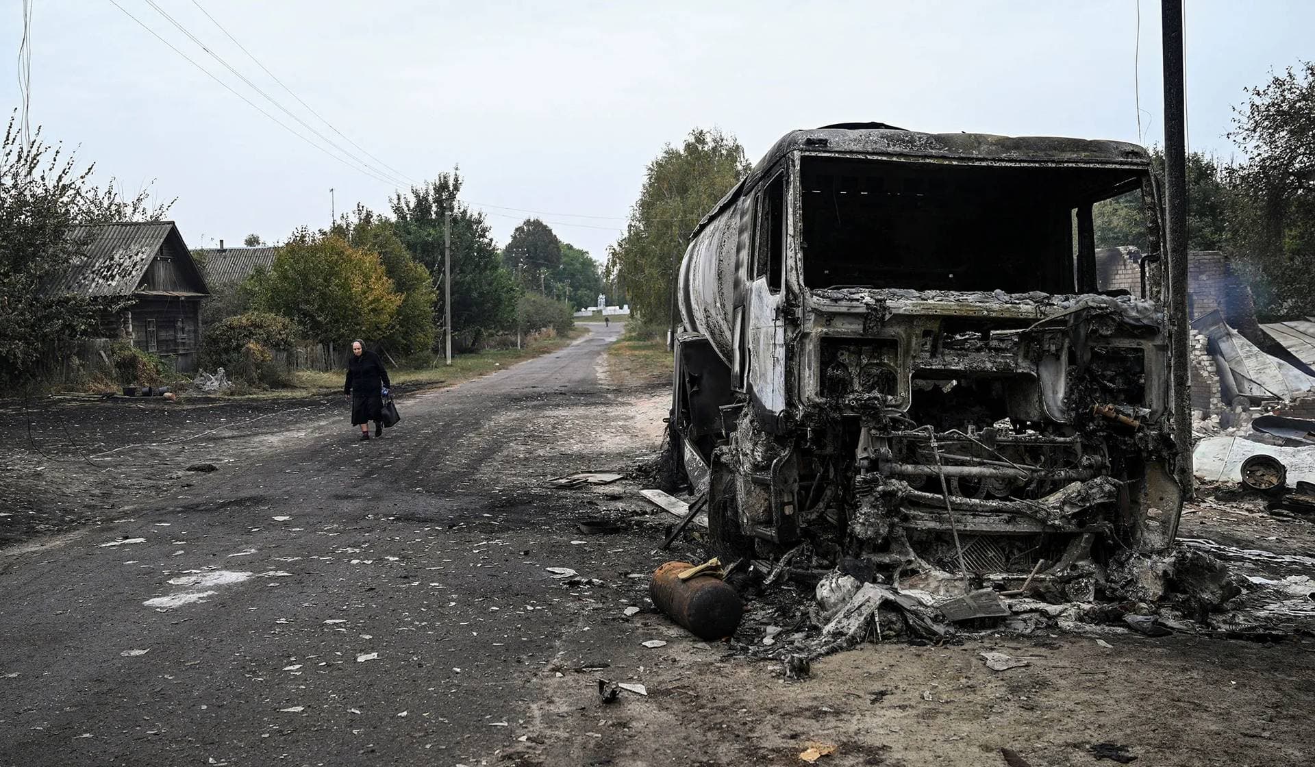 A woman walks near a truck destroyed during a Russian military strike in Hirske