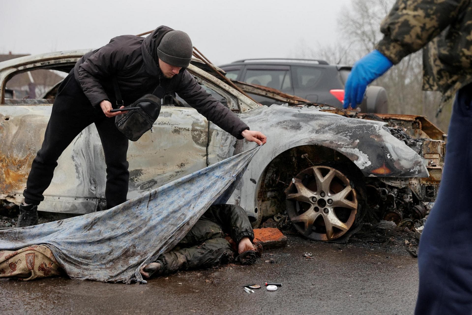 funeral service worker uncovers a civilian's body as Russia's attack on Ukraine continues, in the village of Nova Basan, Chernihiv region