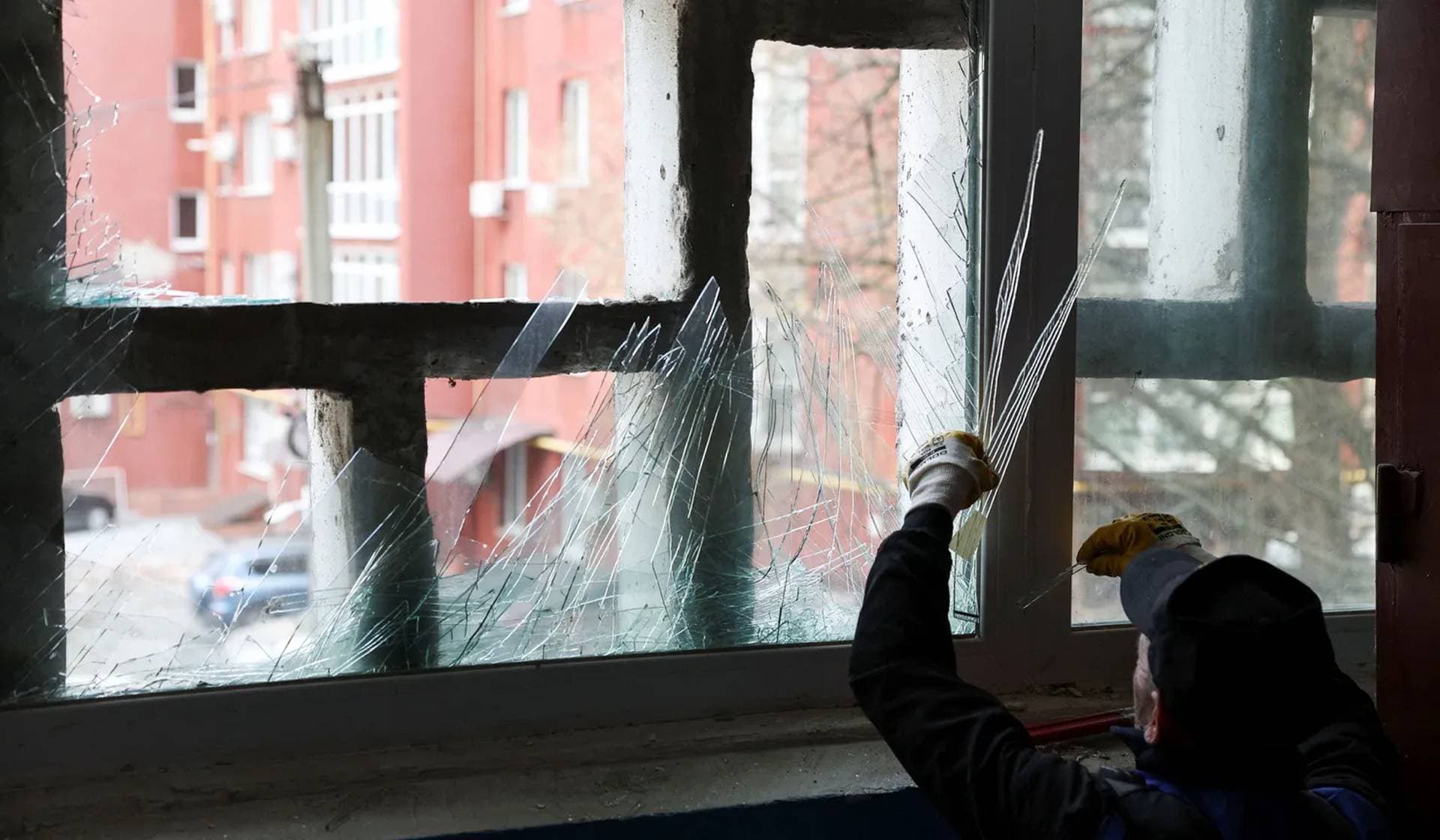 A worker removes shattered glass from a window damaged during an overnight Russian drone strike in a residential neighborhood in Dnipro