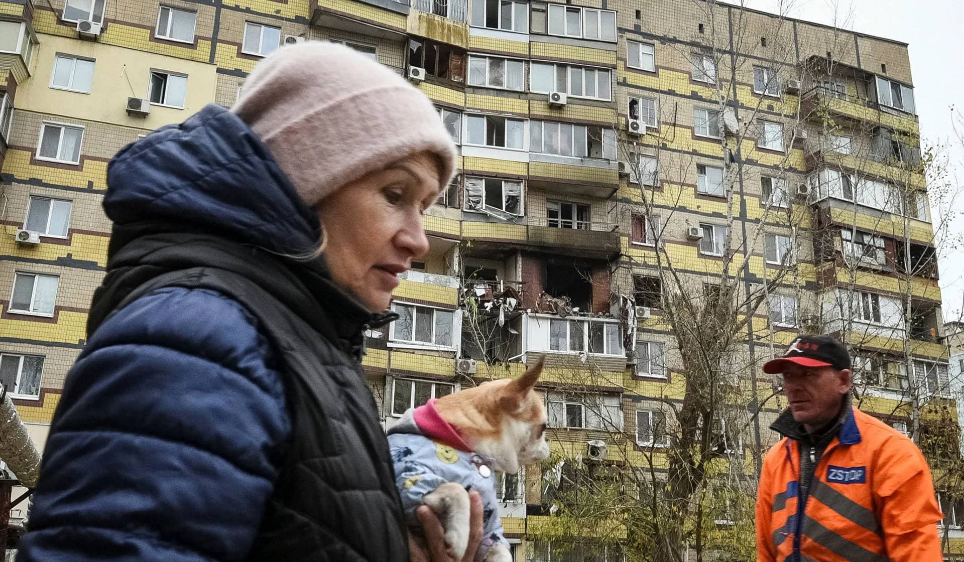 A woman with a dog walks near an apartment building hit during a Russian drone strike in Dnipro
