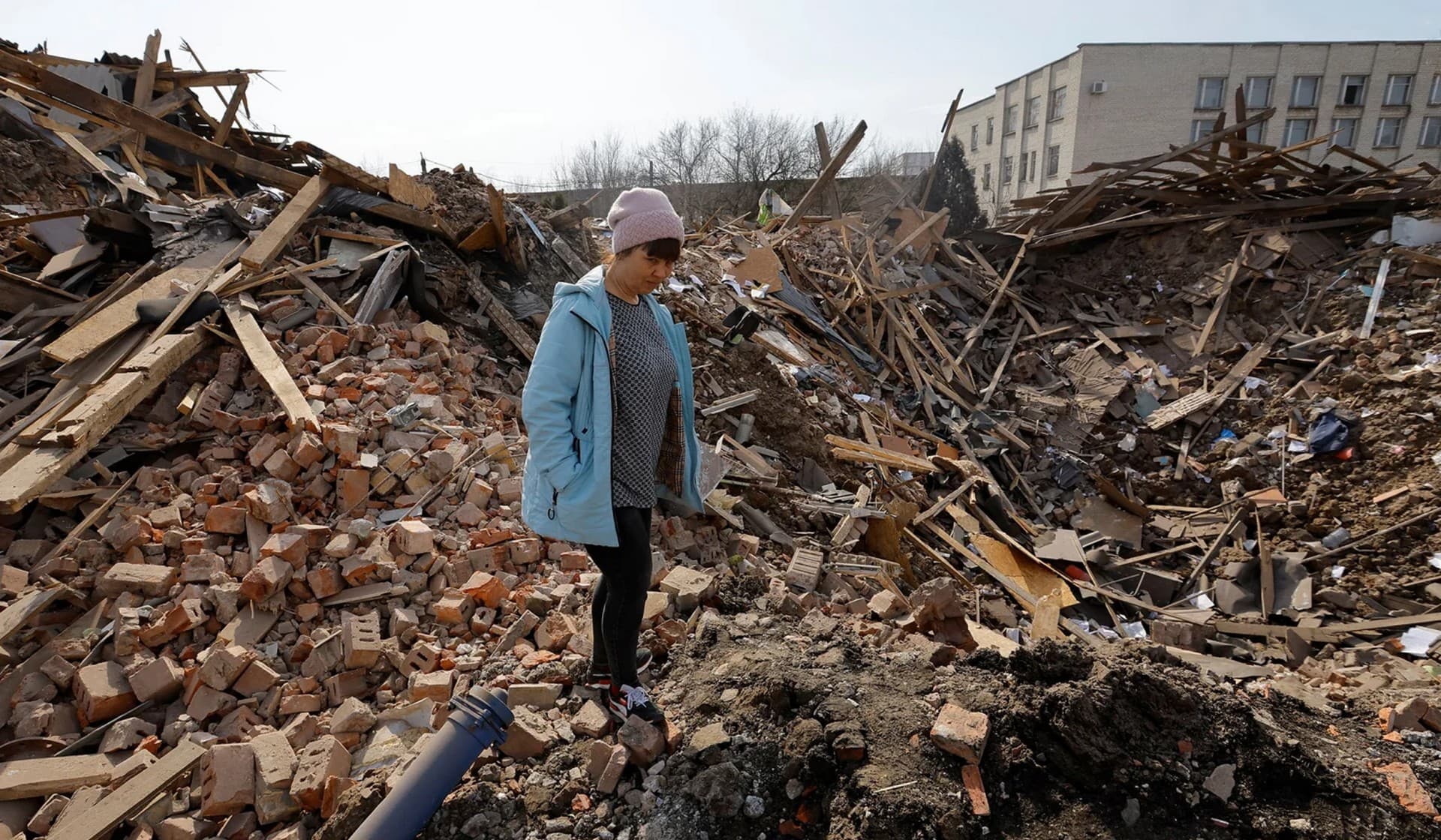 A woman stands next to a shell crater in the ruins of the water supply station building destroyed by recent shelling in Donetsk