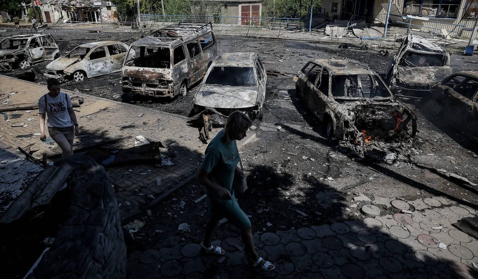 Residents walk past burned cars hit by a Russian drone strike in Druzhkivka