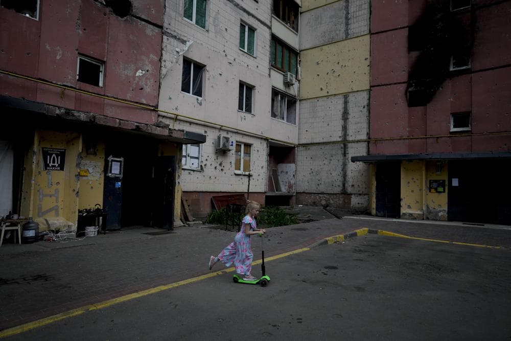 A girl rides a scooter near destroyed buildings during attacks in Irpin