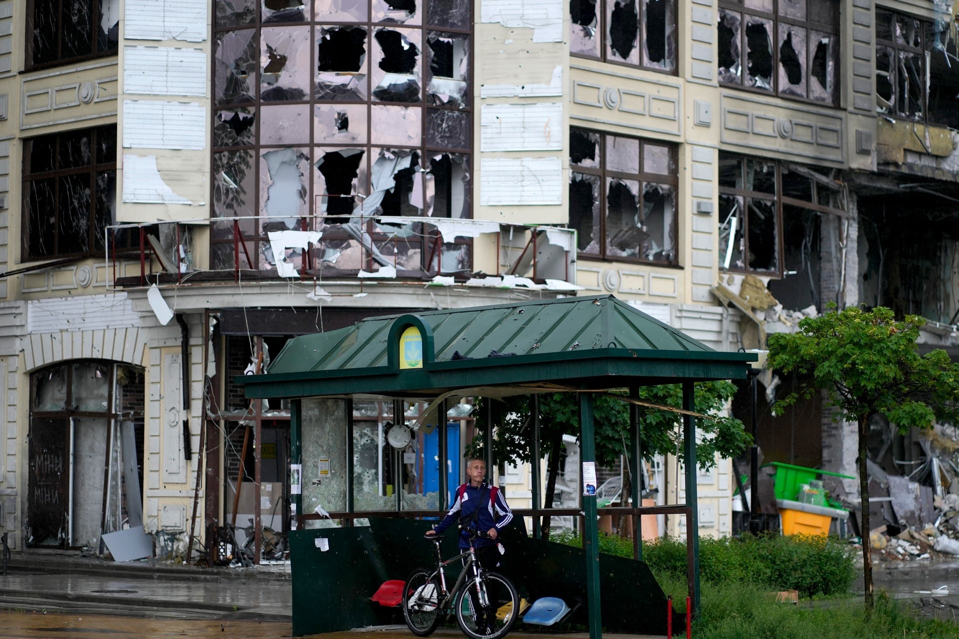 A man stands sheltering from the rain at a bus stop near destroyed building during attacks in Irpin