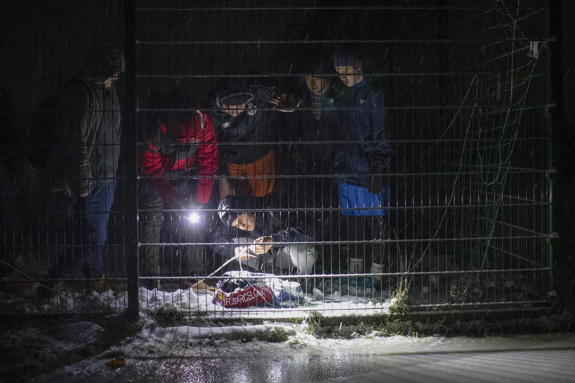 Men connect a homemade light with a battery to illuminate the pitch ahead of a soccer game during a blackout in Irpin