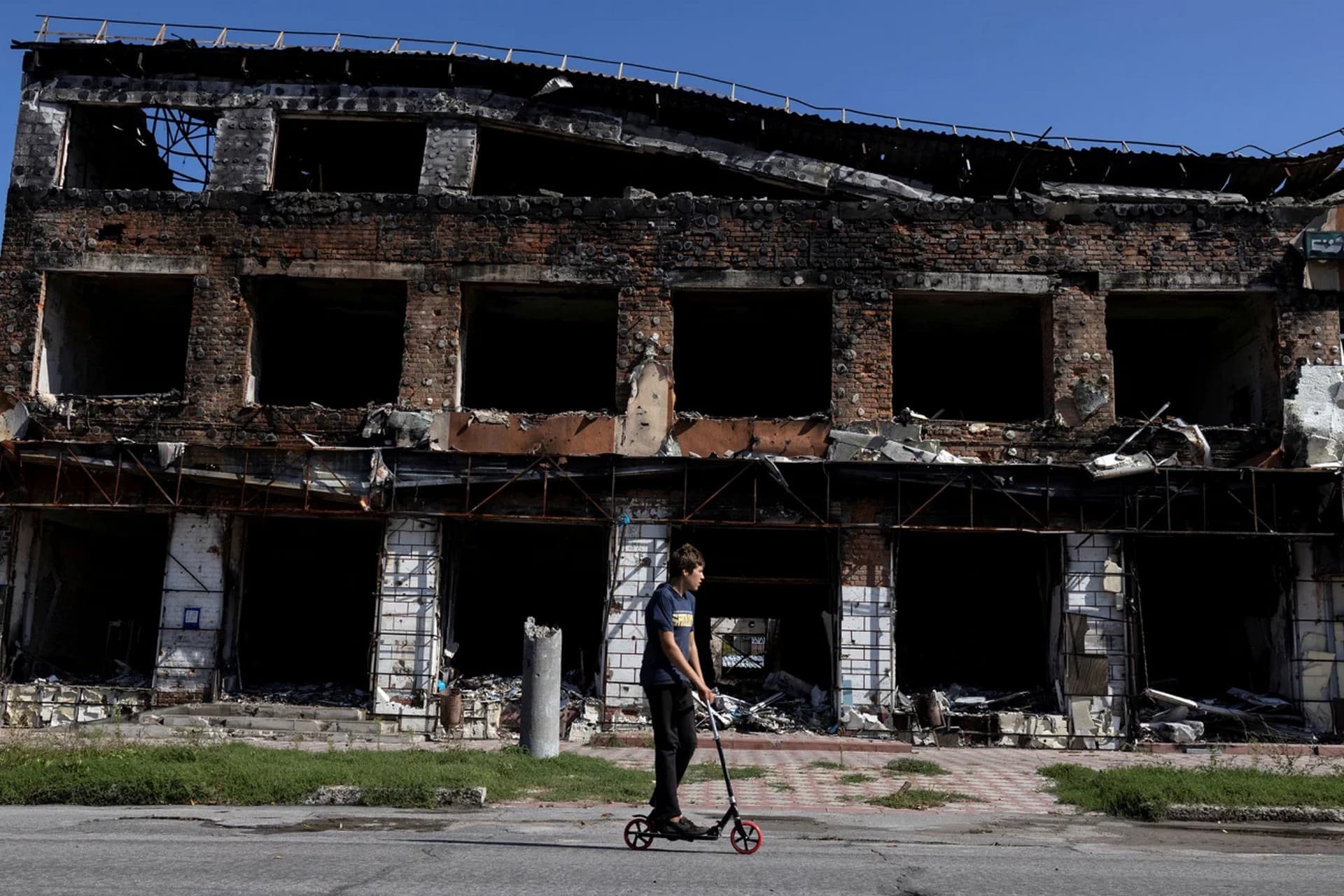 A boy rides his scooter past a destroyed building in the town of Izium