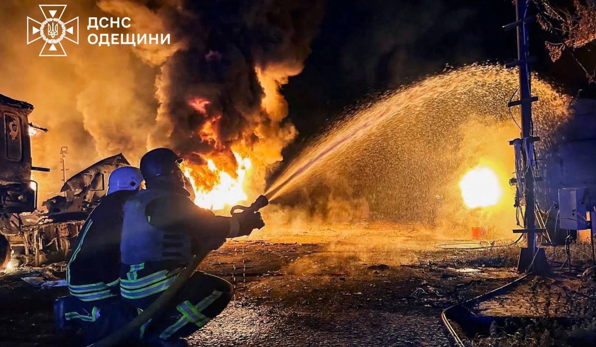 Members of emergency services use a water hose as flames and smoke rise in the aftermath of a Russian drone strike in a location given as Izmail