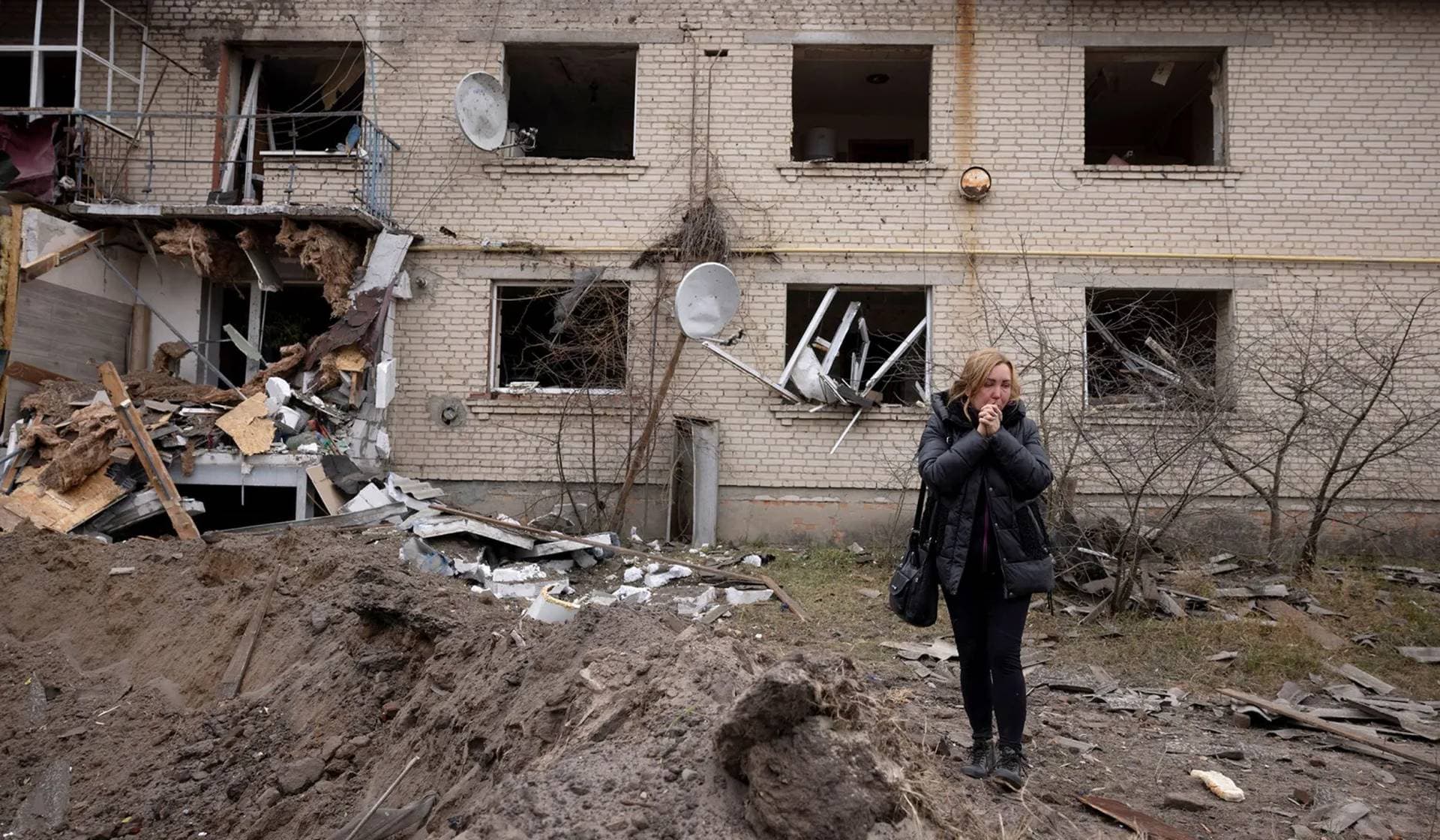 A local woman reacts as she stands at the impact crater of a Russian S-300 missile that hit next to an apartment building in Peresichne