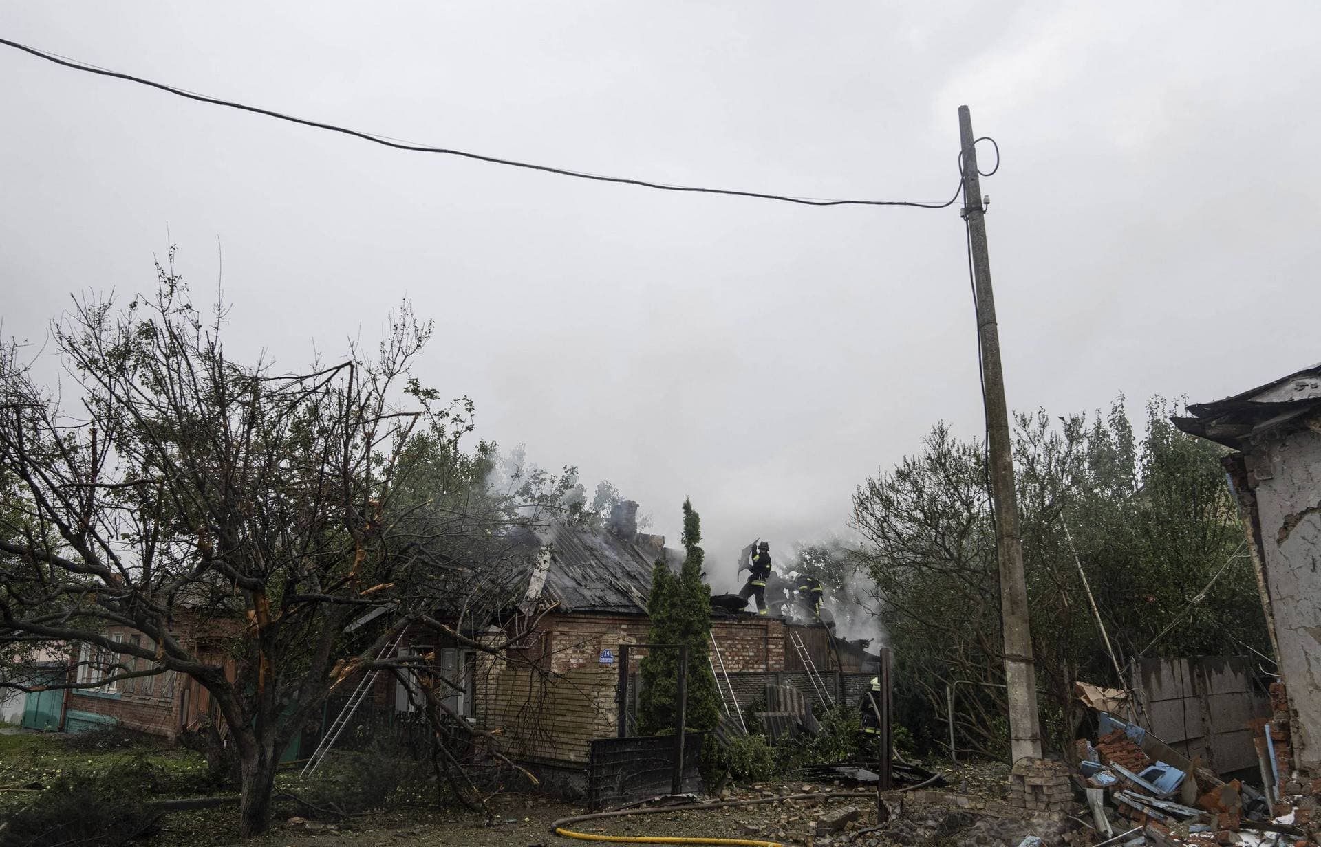 Rescue workers put out the fire of a destroyed car after a Russian attack in a residential neighborhood in downtown Kharkiv