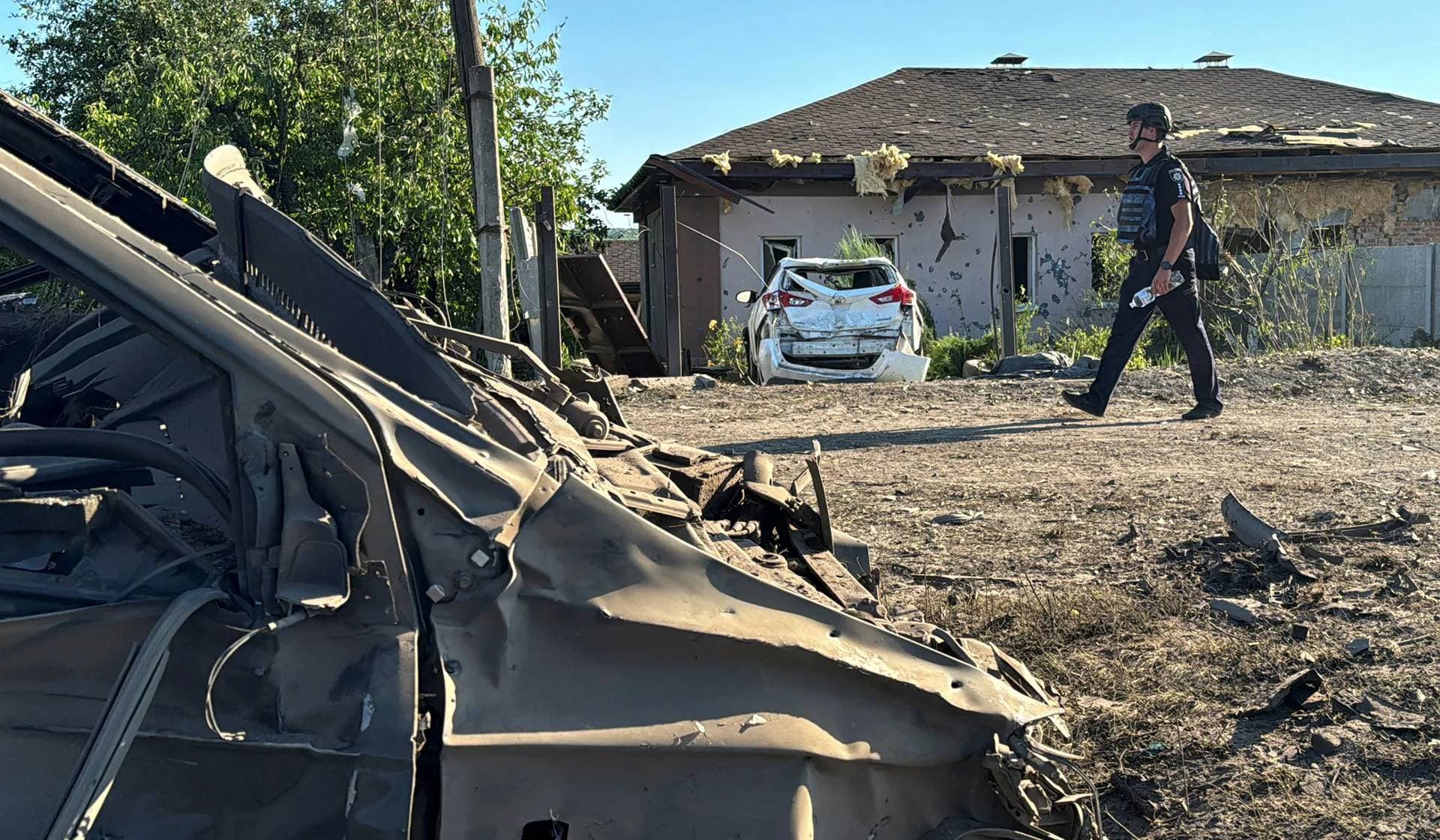 A police officer walks near damaged cars at the site of a Russian missile strike in the village of Budy, Kharkiv Region, Ukraine, July 13, 2024. 