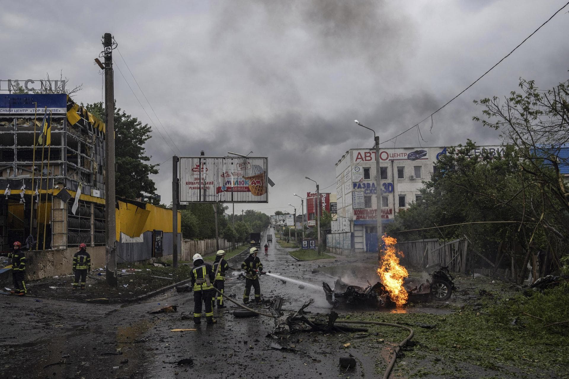 Rescue workers put out the fire of a destroyed car after a Russian attack in a residential neighborhood in downtown Kharkiv