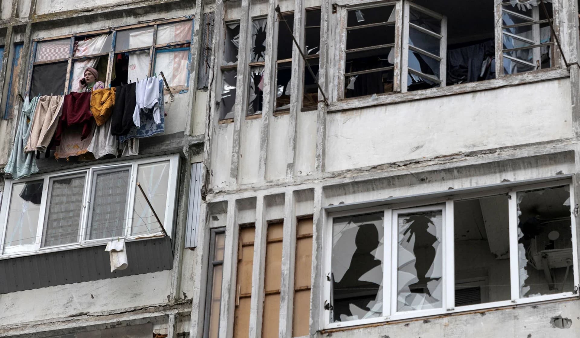 A local woman speaks on her mobile phone in a window of a residential building damaged by a Russian military strike in Kherson