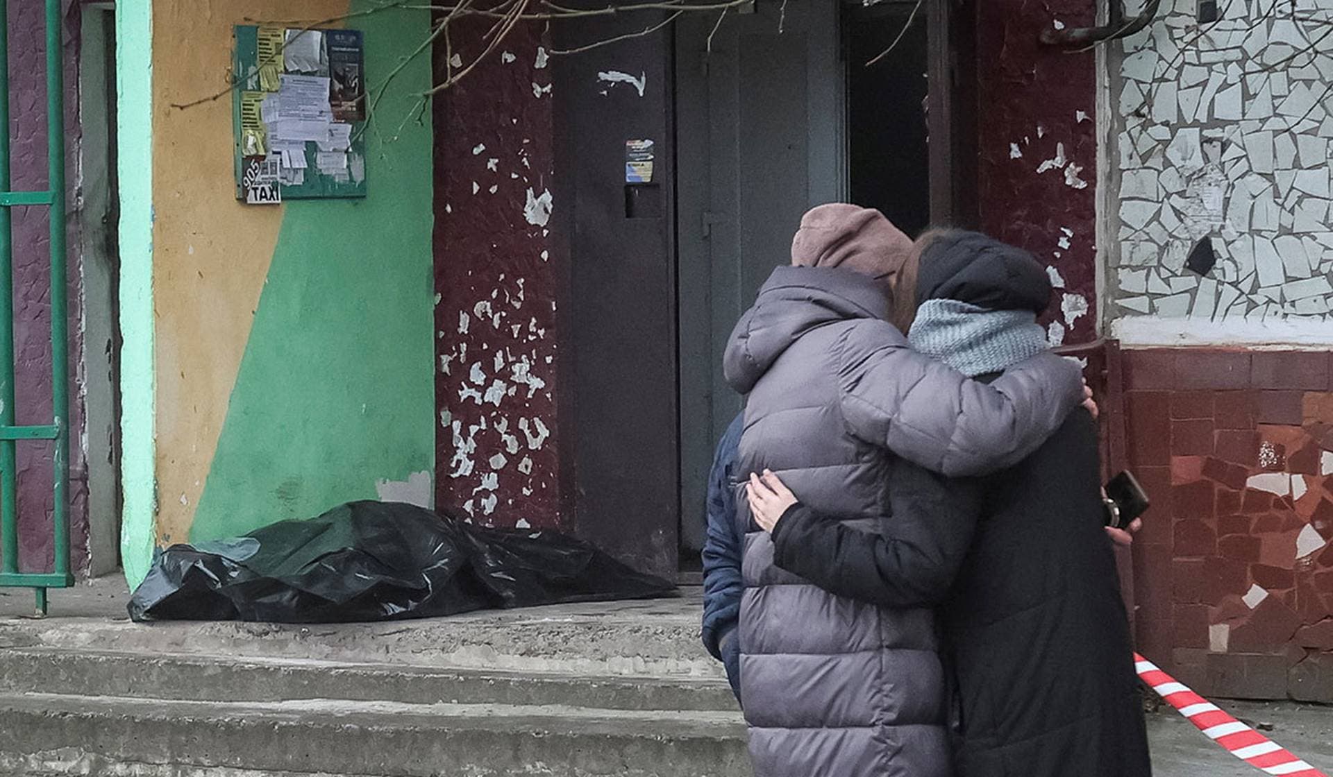Residents react as they stand near the body of a person found dead at an apartment building hit by a Russian drone strike, which happened late evening on Monday in Kramatorsk