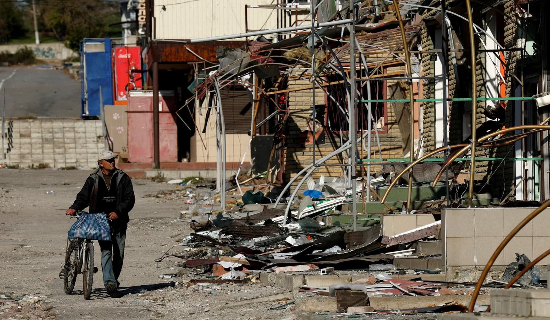 A man walks with his bicycle through a destroyed shopping street in town of Kupiansk