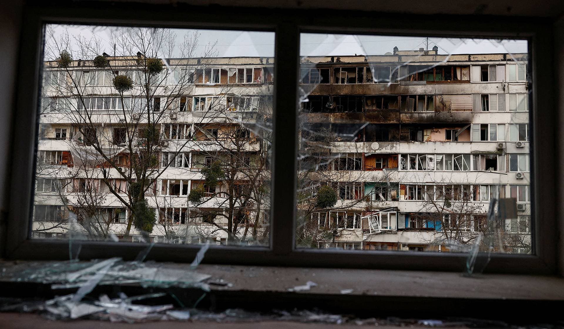 An apartment building hit by a Russian drone strike seen through a broken window in Kyiv