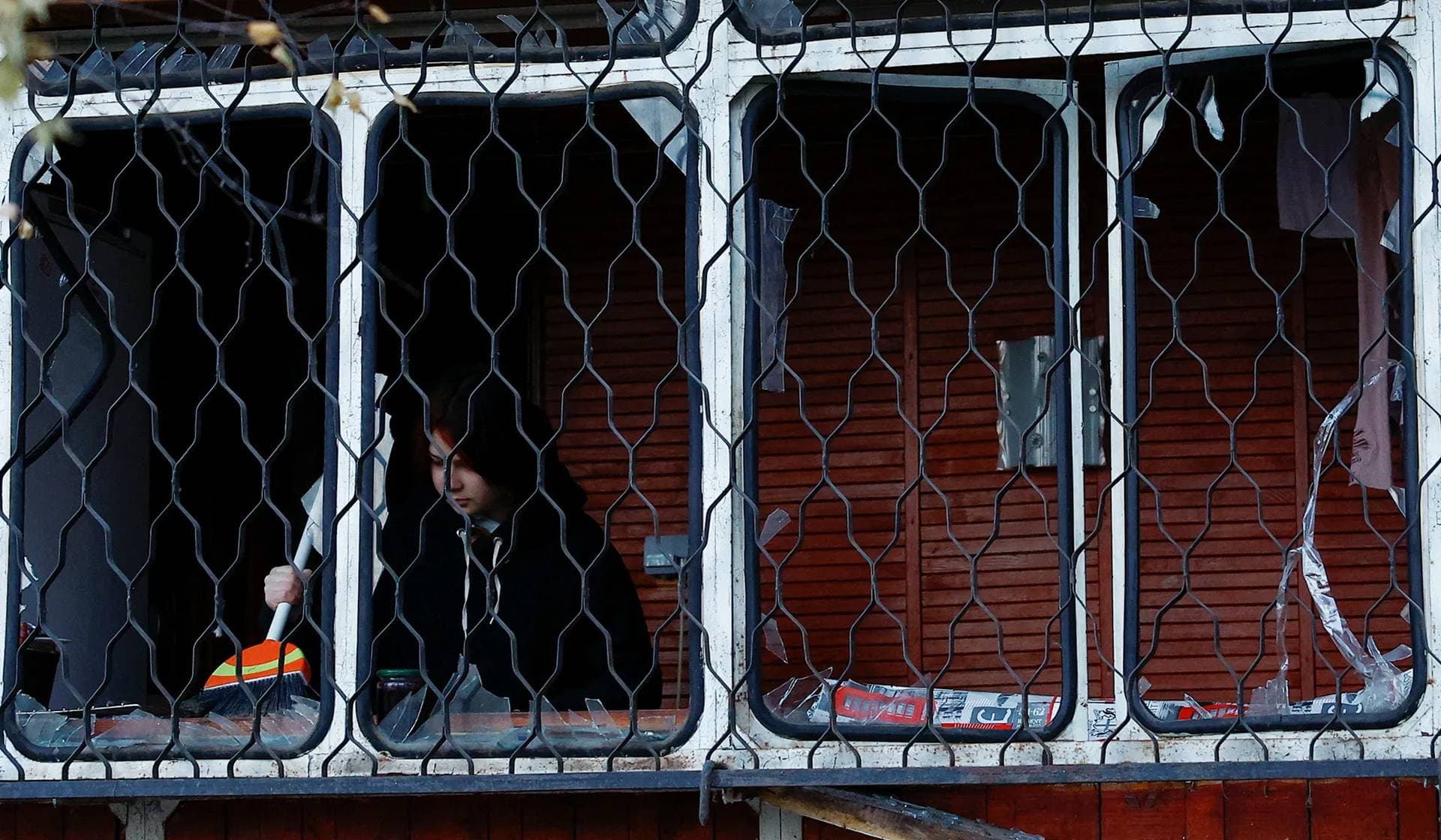A local resident removes debris at a balcony of her apartment damaged during Russian drone strikes in Kyiv