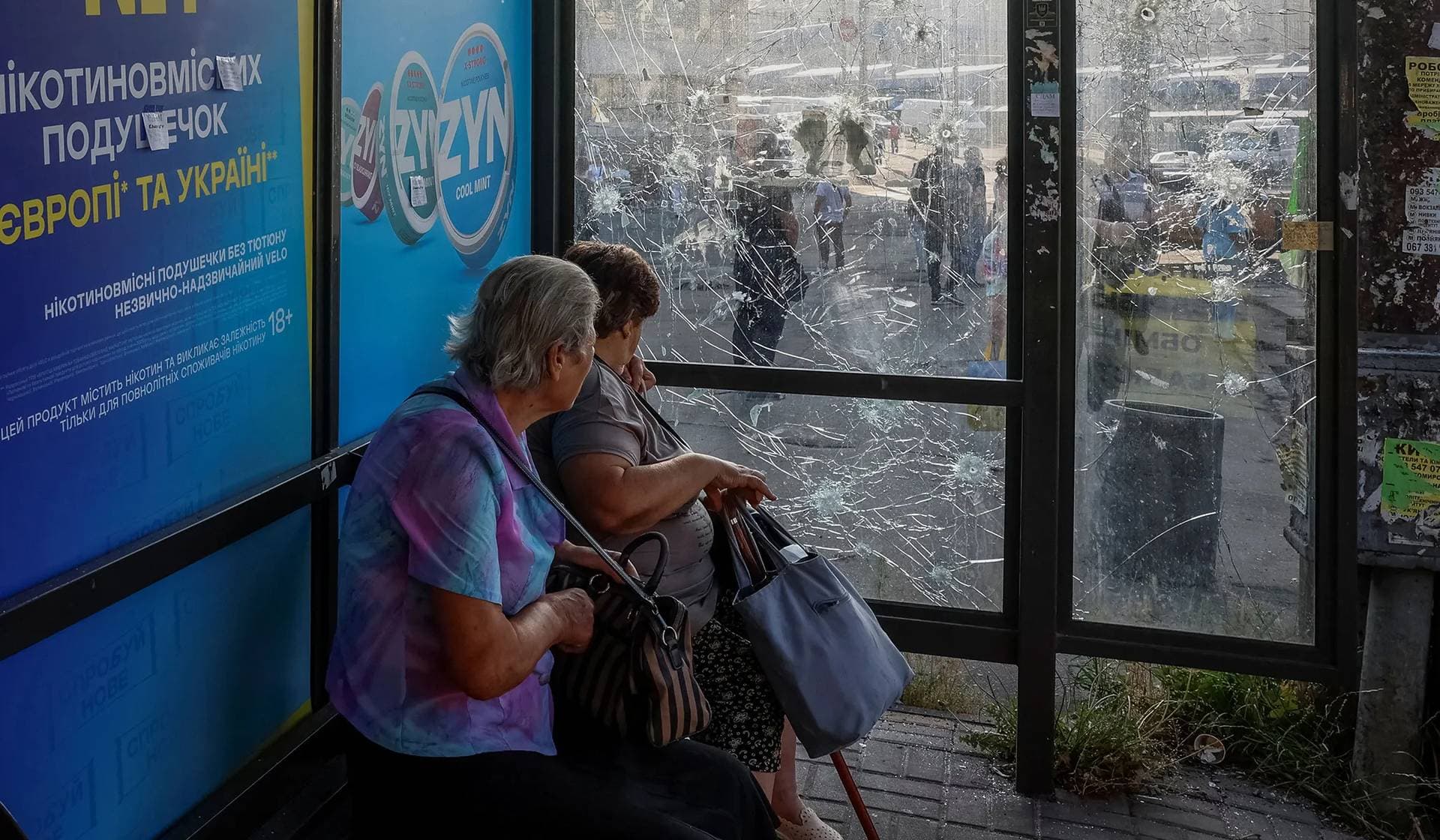 Women sit at a bus stop damaged during Russian drone and missile strikes in Kyiv