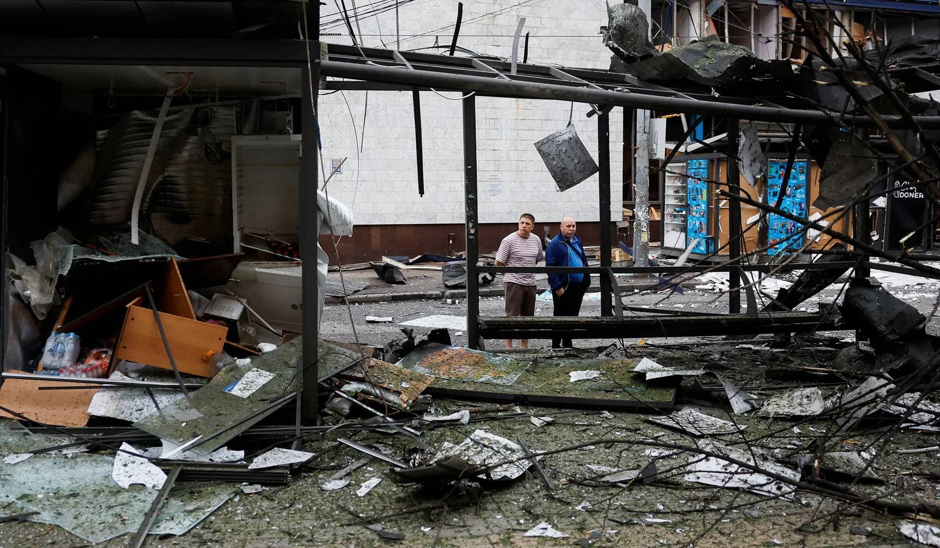 People look at a damaged bus stop outside the metro station that was damaged during the night due to Russian drone and missile strikes in Kyiv