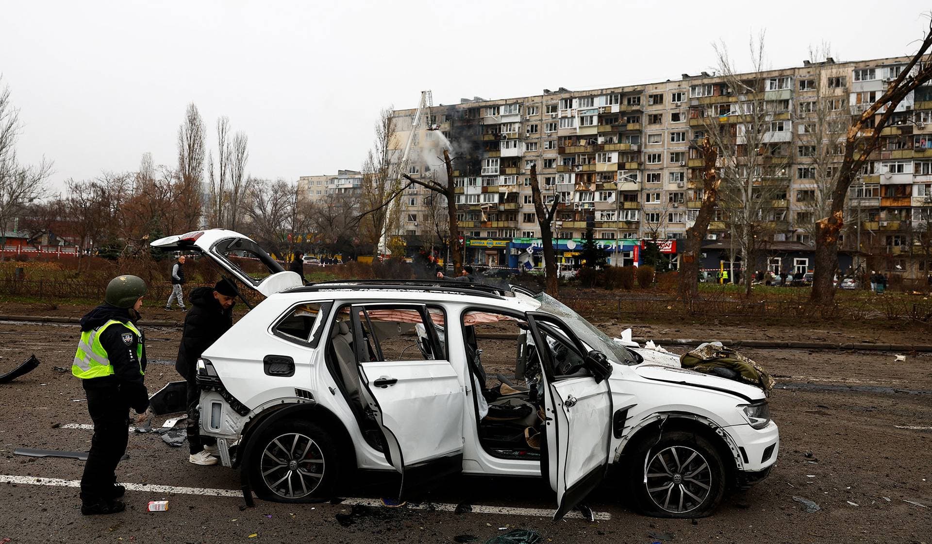 People inspect a damaged car, in the aftermath of a Russian missile and drone attack on Kyiv