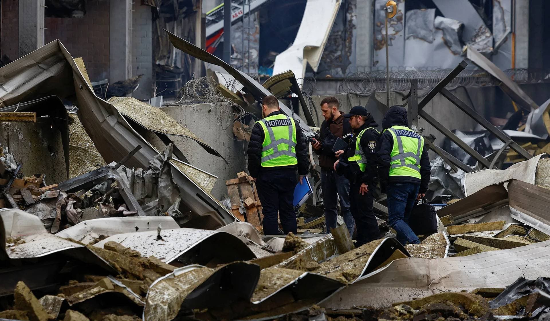 Police investigators stand next to the body of a person found among debris at the site of food warehouses hit by an overnight Russian missile strike in Kyiv
