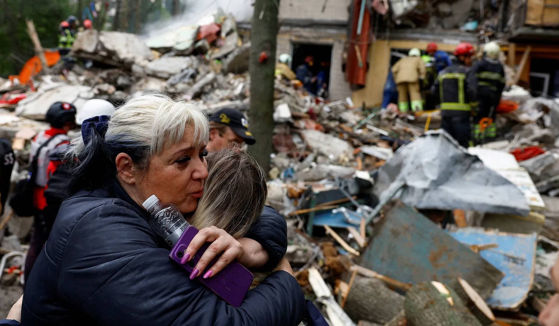 A woman embraces a person as she waits for her son to be rescued from under the debris at the site of an apartment building hit during Russian missile and drone strikes in Kyiv