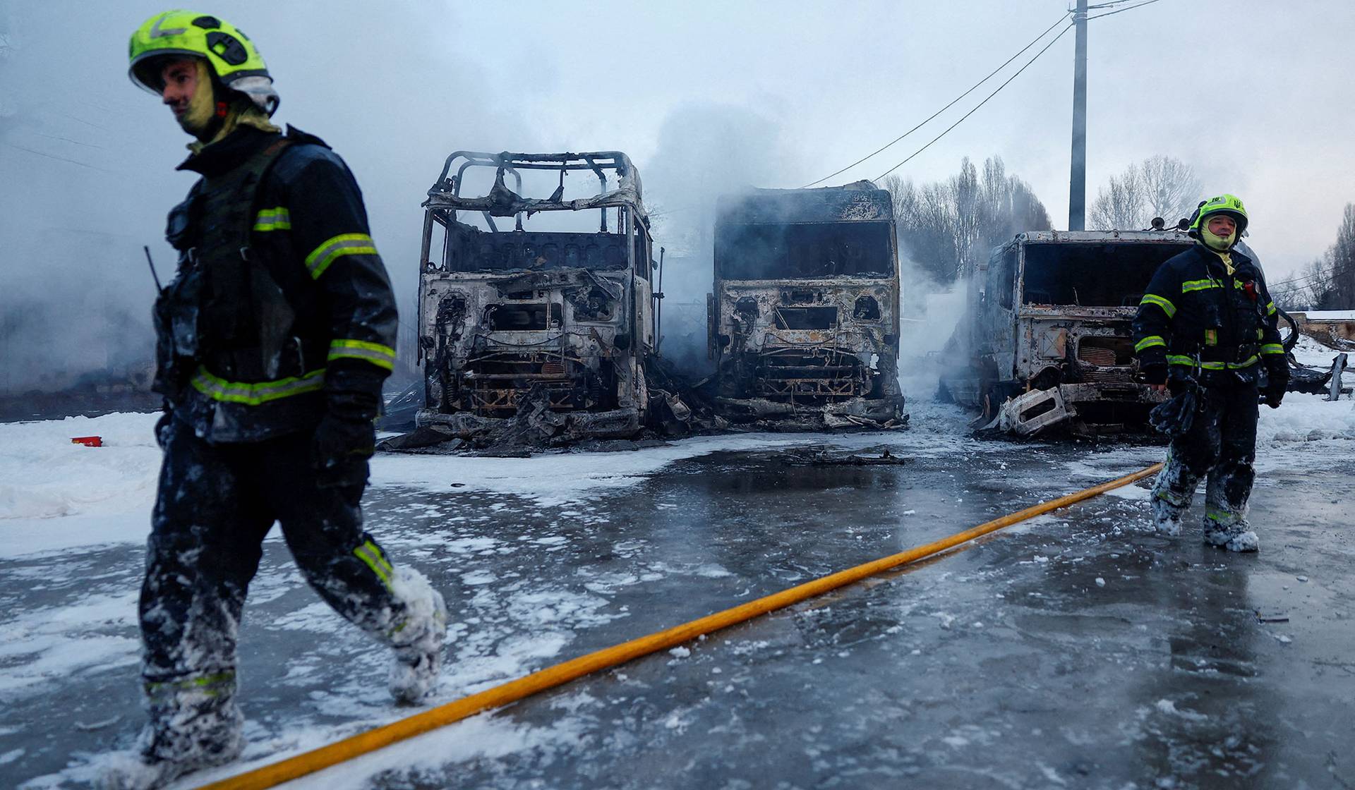 Firefighters walk in front of semi-trucks destroyed during overnight Russian drone and missile strikes in Kyiv