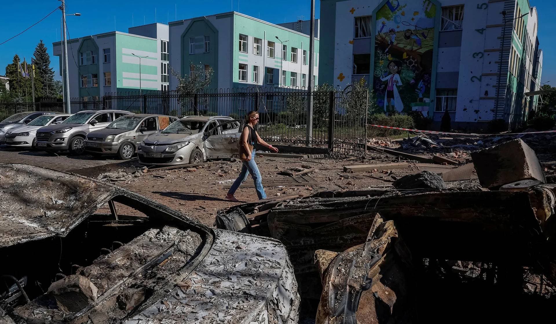A woman passes by destroyed vehicles at the site of a school hit during Russian drone and missile strikes in Kyiv