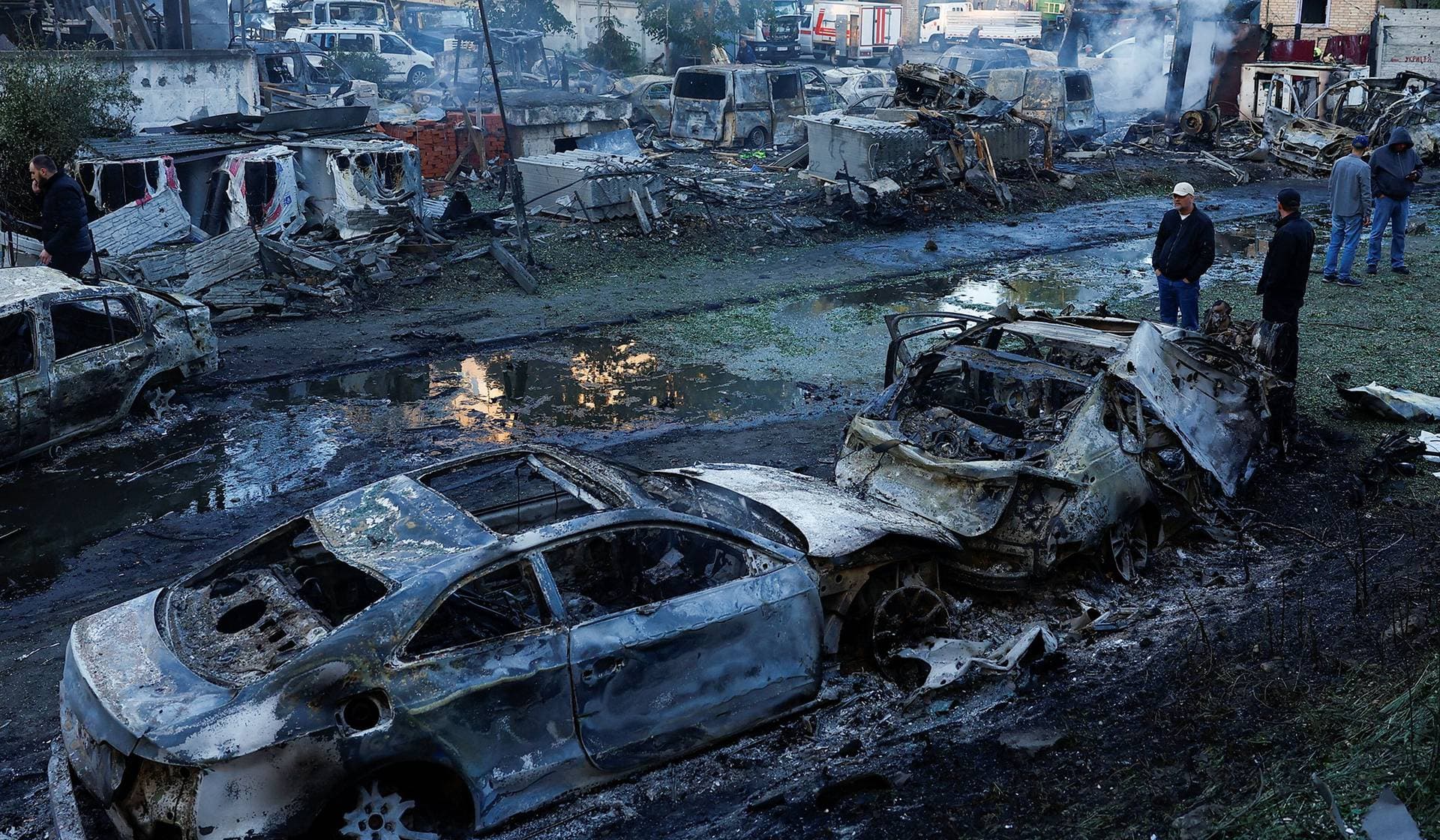 People look at cars damaged during Russian missile and drone strikes at a garage in Kyiv
