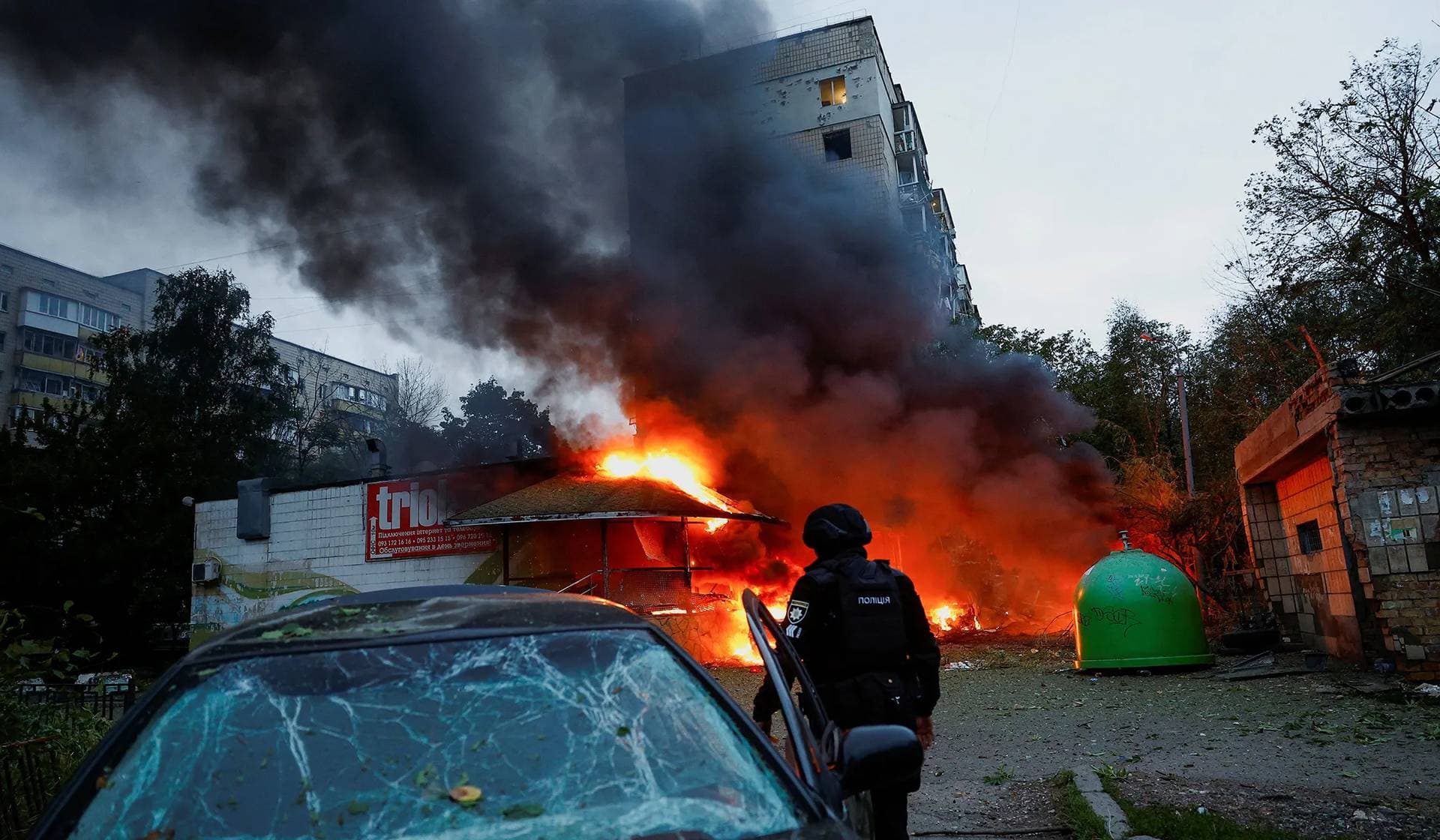 Cars damaged during Russian missile and drone strikes burn next to an apartment building also damaged during the strikes in Kyiv