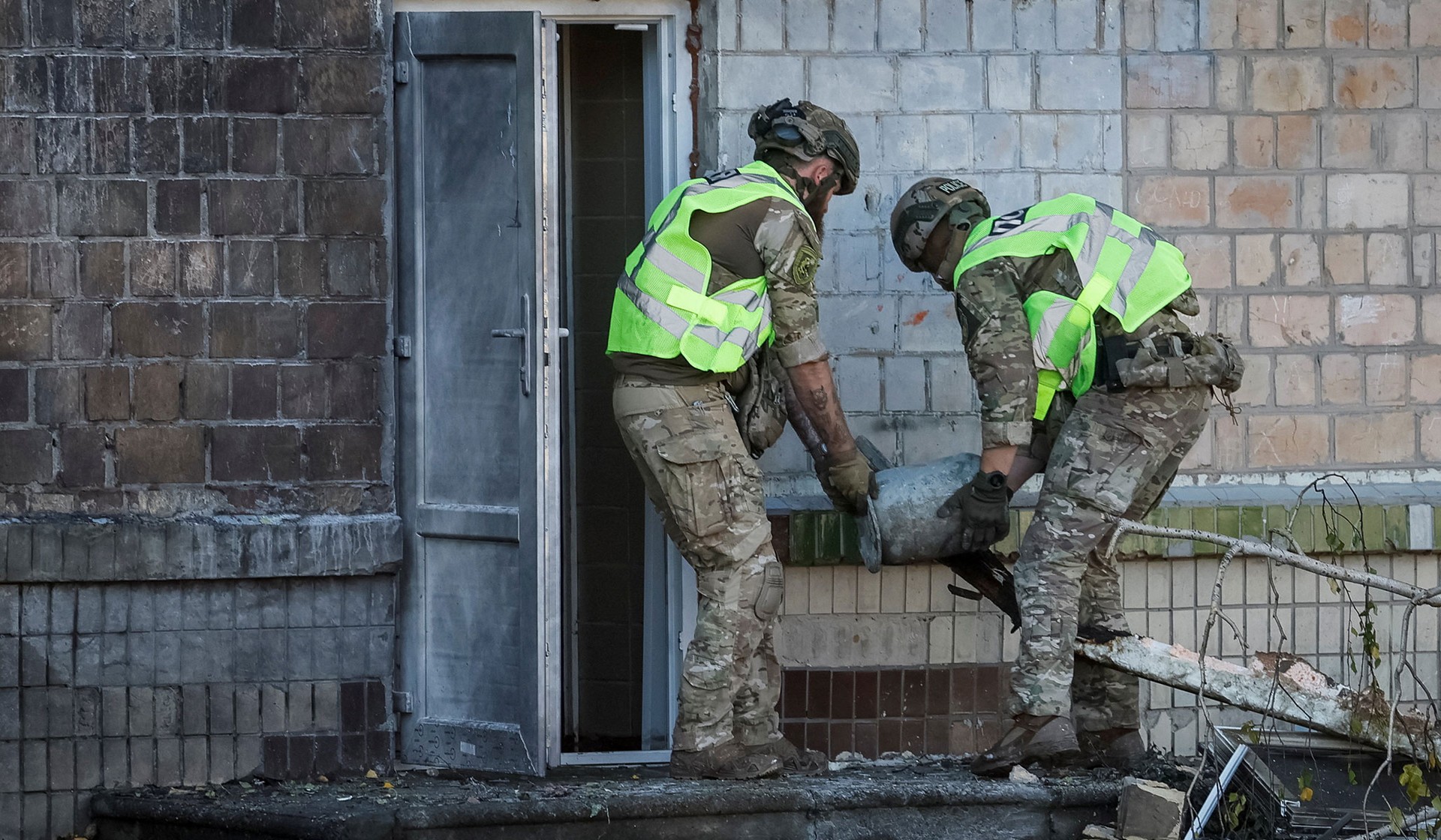 Police bomb squad members carry an unexploded Russian drone warhead at a site of a damaged school hit by a Russian jet-drone strike in Kyiv