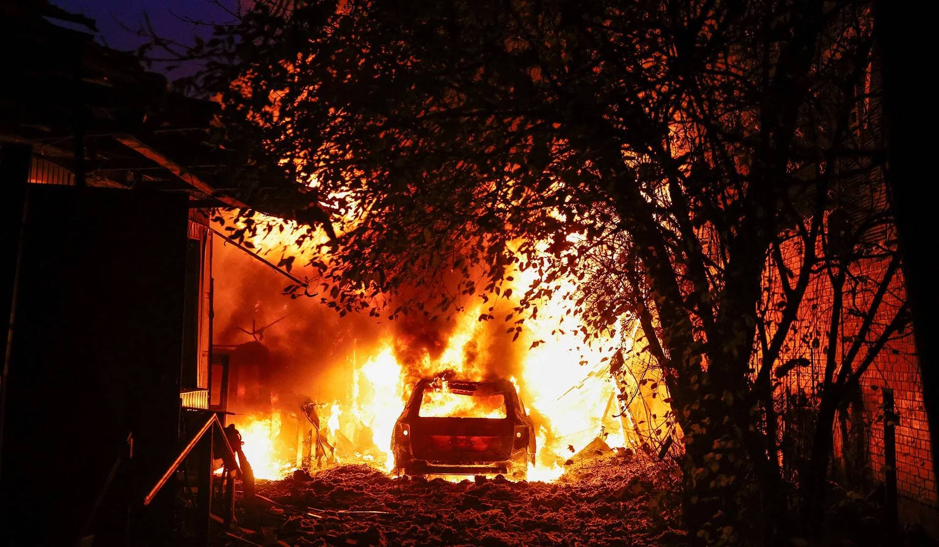 A car and private house burn after they were damaged during a Russian drone strike in Kyiv