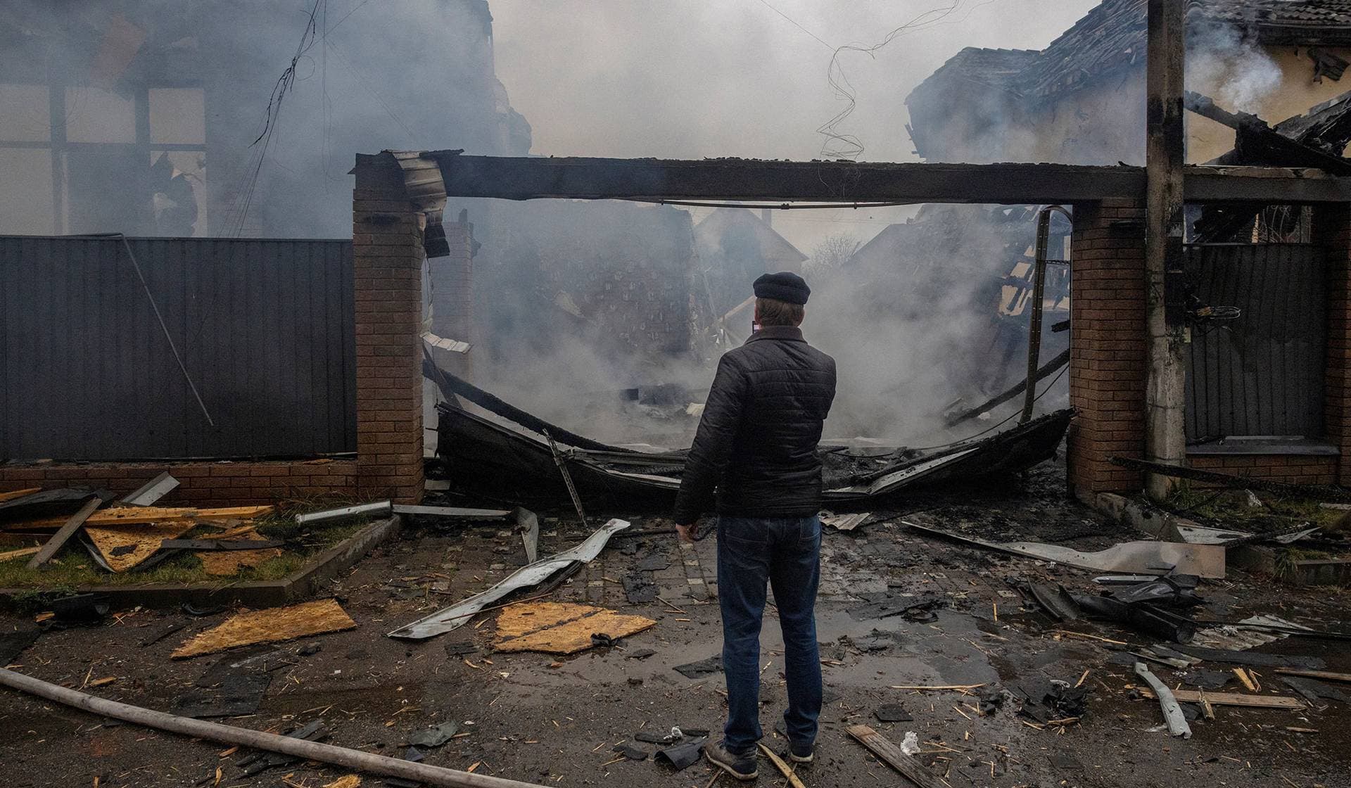 A neighbour looks at a private home that went up in flames after it was hit by a Russian drone during a night of attacks on Kyiv