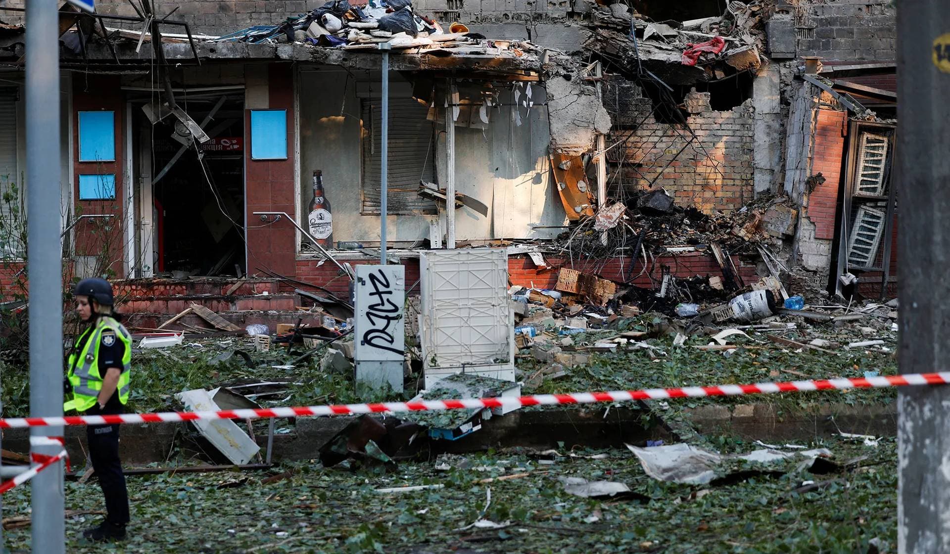 A member of the emergency services stands behind a cordon at a building, damaged during Russian drone and missile strikes in Kyiv