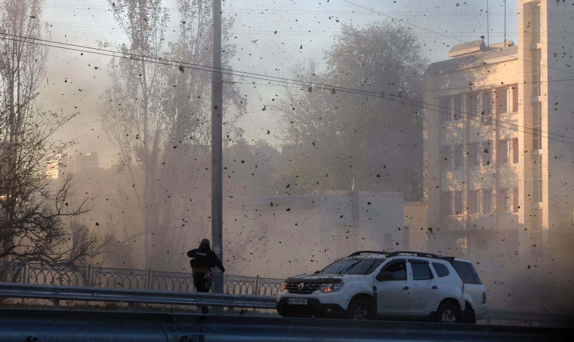 A police officer watches stone and earth debris flying through the air as Russian kamikaze drones hit the centre of the capital Kyiv