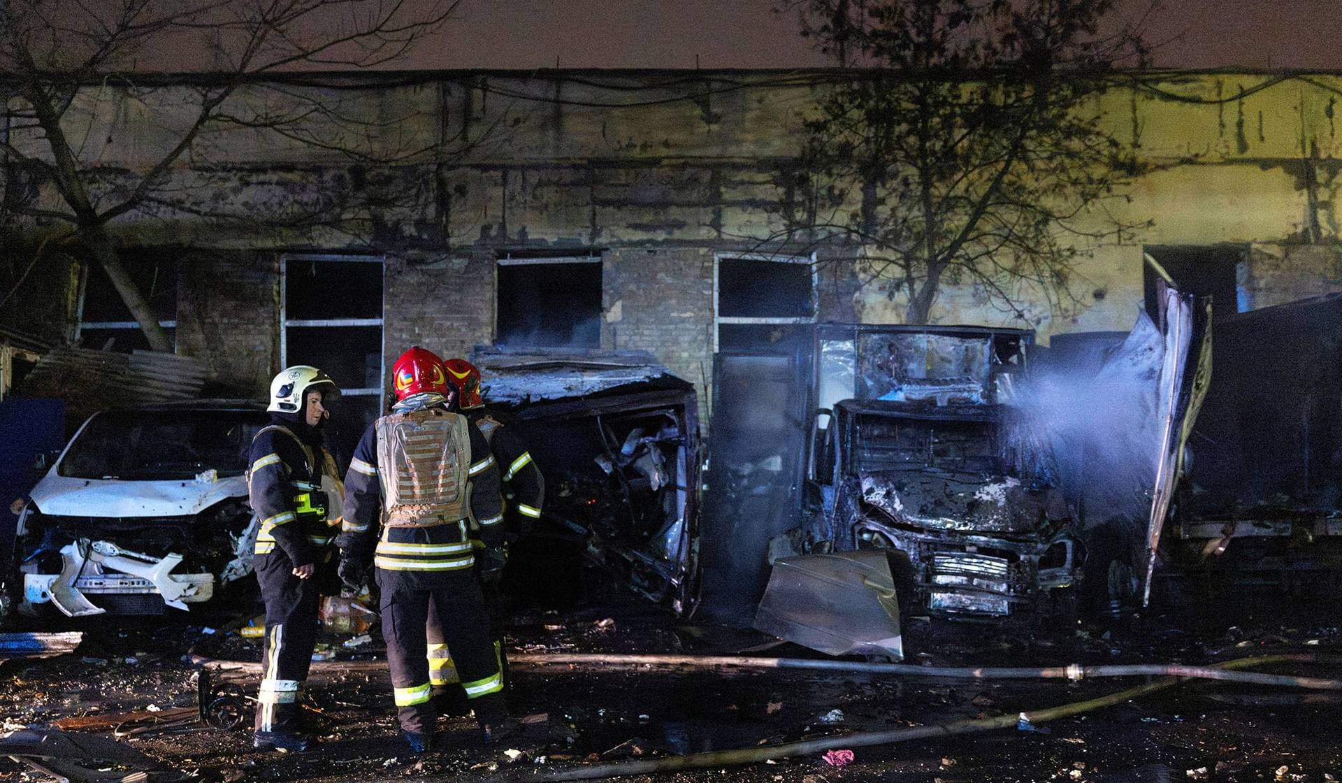 Firefighters stand near burned-out cars at an impact site after a Russian drone attack in Kyiv