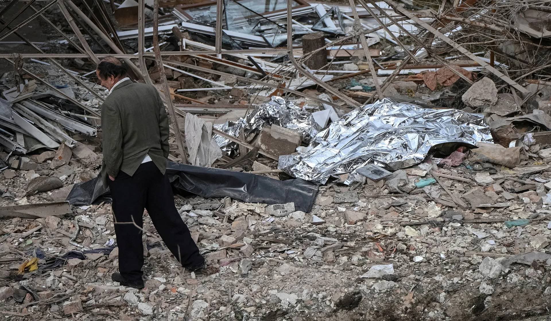 A man walks near the covered bodies of the victims of a Russian drone and missile strike lying near their destroyed house in the village of Lapaivka